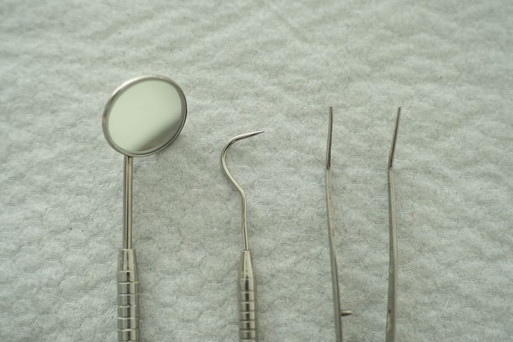 Close-up of dental tools including mirror and pick on a gray textured background.