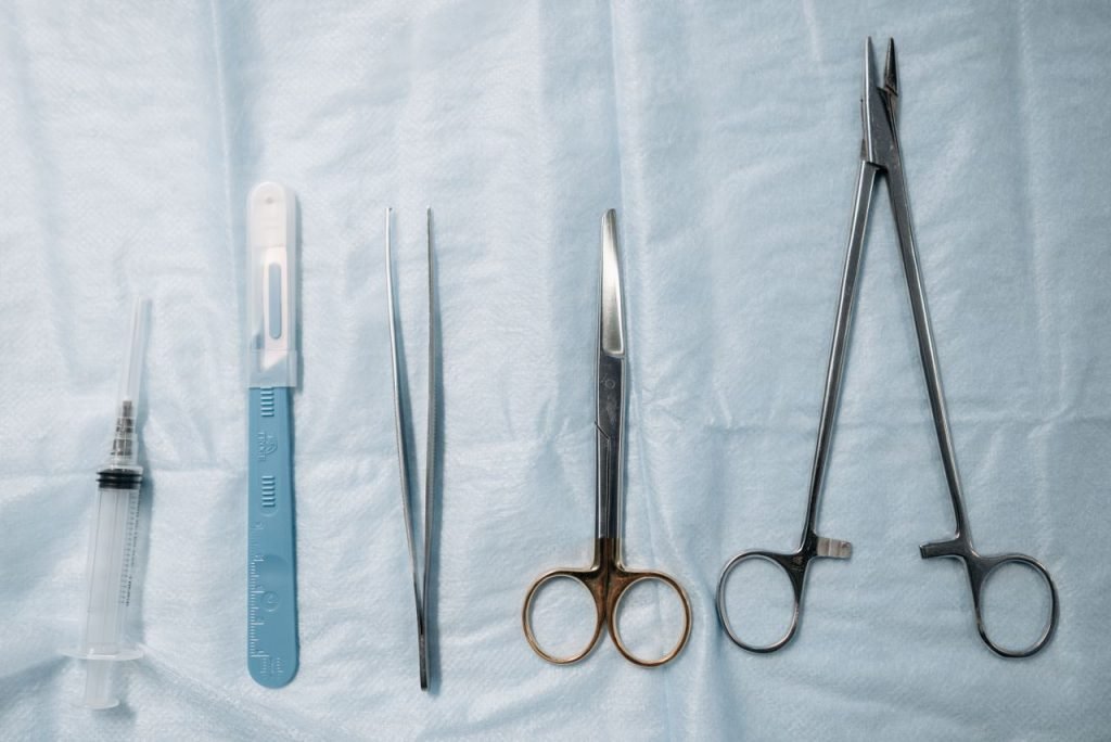 Flat lay of surgical tools including scissors, forceps, and syringe on a sterile blue cloth.